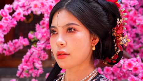 Primer-Plano-De-Una-Mujer-De-La-Dinastía-Qing-Con-Flores-Rosadas-En-El-Fondo.