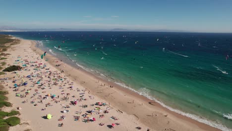 Video-Aéreo-De-Kitesurfistas-Practicando-Y-Gente-Disfrutando-De-La-Playa-Durante-El-Día-Soleado-En-La-Playa-De-Tarifa,-Cádiz,-España.