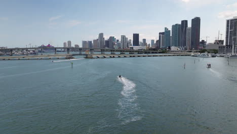 Aerial-view-following-water-scooter-and-boats-moving-toward-the-Miami-skyline,-USA