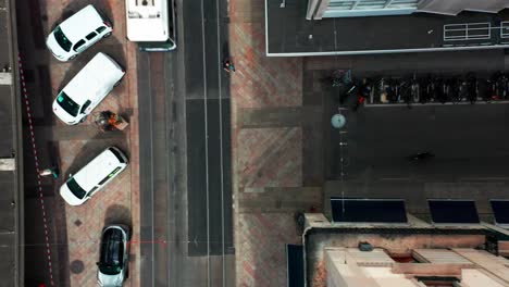Top-down-aerial-of-tram-driving-over-a-small-street-while-the-drone-flies-over-the-facade-of-an-historical-building