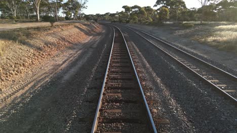 Drone-flying-at-low-altitude-over-train-rails-in-rural-landscape