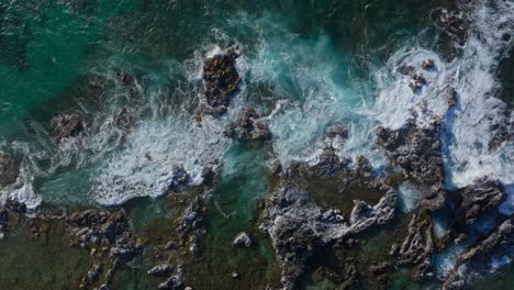 Aerial-overhead-pan-of-ocean-waves-washing-over-coastal-rocks,-Hawaii