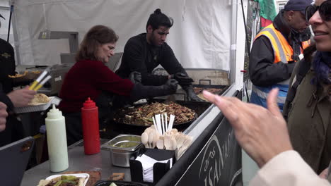 An-Einem-Stand-Wird-Den-Leuten-Essen-Serviert,-Während-Eine-Frau-Beim-Jährlichen-Eid-Festival-Des-Londoner-Bürgermeisters-Auf-Dem-Trafalgar-Square-Fleisch-Und-Gemüse-Auf-Einer-Heißen-Platte-Mischt