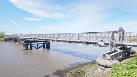 Caminantes-Cruzando-El-Puente-Peatonal-Y-El-Oleoducto-Sobre-El-Río-Tidal-Blyth,-Sendero-Para-Caminar-En-Suffolk