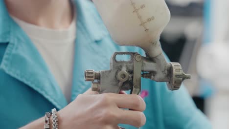 Worker-using-spray-gun-for-shoe-finishing-in-factory,-close-up-of-hands-and-equipment