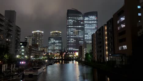 El-Horizonte-De-La-Ciudad-Iluminado-Por-La-Noche,-Reflejándose-En-El-Río,-Creando-Una-Atmósfera-Urbana-Serena