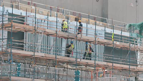 Workers-labouring-on-a-suspended-platform-at-a-construction-site-during-a-hot-summer-day-in-Dubai,-United-Arab-Emirates