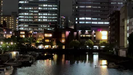 Nachtansicht-Der-Beleuchteten-Stadtgebäude,-Die-Sich-Im-Wasser-Spiegeln