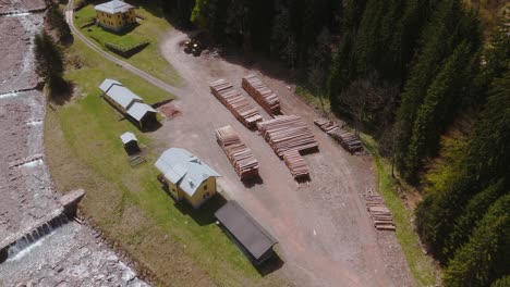 A-sawmill-in-a-forested-area-with-stacks-of-cut-logs-and-buildings-visible,-aerial-view