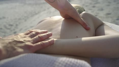 Tattooed-therapist-giving-a-relaxing-massage-on-a-beach-in-the-sunlight,-close-up