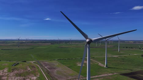 Wind-turbines-spinning-on-a-sunny-day-in-a-wide-open-green-field,-aerial-view