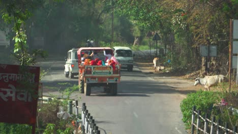 Eine-Gruppe-Von-Dorfbewohnern-Reist-In-Einem-Traktorwagen-Durch-Eine-Indische-Straße,-Vorbei-An-Verkehr-Und-Kühen