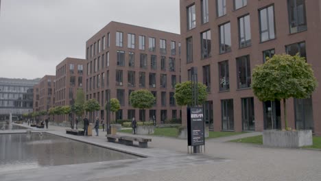 Modern-business-district-with-brick-buildings-and-lush-trees-on-a-cloudy-day,-people-walking-and-sitting