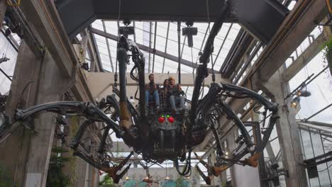 In-the-steampunk-park,-a-spider-hangs-from-the-ceiling-and-carries-people-on-its-back