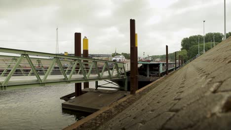 Static-shot-of-a-green-bridge-over-water-with-a-cloudy-sky-and-industrial-backdrop,-wooden-foreground-detail
