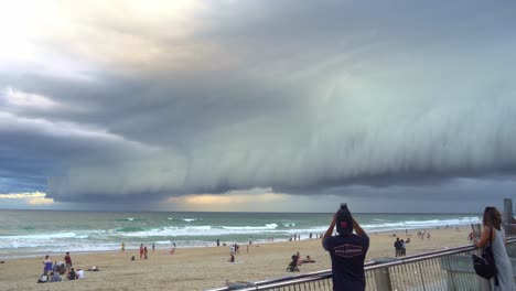 People-gathered-at-Surfers-Paradise-beach,-Gold-Coast,-observing-a-dramatic-apocalyptic-scene-unfolding-in-the-sky,-characterized-by-thick-layers-of-ominous-clouds-sweeping-across-the-horizon