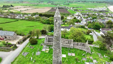 Irlanda-Lugares-épicos-Drone-Primer-Plano-Rodeando-La-Torre-Redonda-De-Ardmore-Y-La-Catedral-Con-El-Pueblo-Costero-De-Ardmore-Al-Fondo-En-Waterford