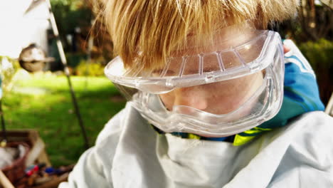 A-young-boy,-wearing-protective-goggles,-uses-a-paint-roller-to-paint-outdoors