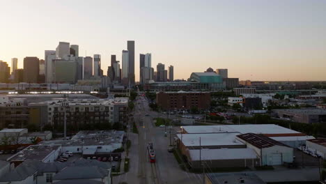 Light-rail-tram-approaching-the-skyline-of-Houston,-sunny-morning---Drone-shot