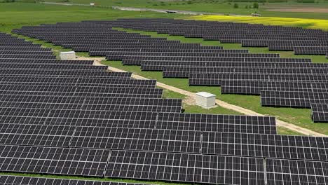 Expansive-solar-panel-farm-in-a-green-field-under-a-clear-sky,-aerial-view