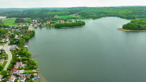 An-aerial-view-of-a-lakeside-town-with-houses-lining-the-water's-edge-and-lush-green-hills-in-the-background