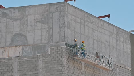 Workers-labouring-on-a-suspended-platform-at-a-construction-site-during-a-hot-summer-day-in-Dubai,-United-Arab-Emirates