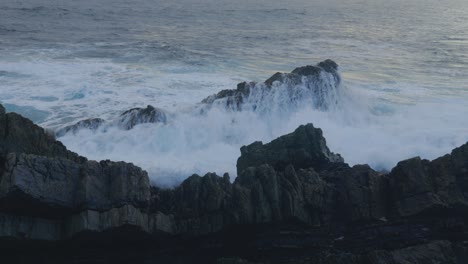 Close-up-slow-motion-shot-of-a-large-wave-crashing-into-a-ruggard-rock-along-the-Australian-coastline