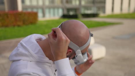Caucasian-man-adjusts-straps-while-wearing-white-VR-headset-outdoors