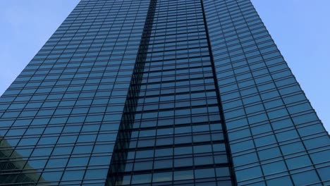 Glasfassade-Eines-Modernen-Wolkenkratzers,-Die-Einen-Klaren-Blauen-Himmel-Und-Benachbarte-Gebäude-Reflektiert