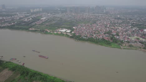 Vista-Aérea-De-Un-Río-Sinuoso-Y-Una-Ciudad-Construida-A-Lo-Largo-De-Sus-Orillas,-También-Hay-Varios-Puentes-Que-Cruzan-El-Río,-Incluido-Un-Puente-Colgante-Rojo