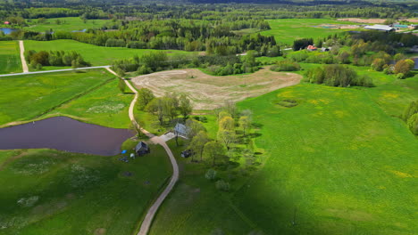 Campo-De-Pueblo-Rural-En-Atmósfera-Verde-Primaveral-Toma-Panorámica-Aérea-De-Drones,-Un-Camino-Entre-Prados-Verdes