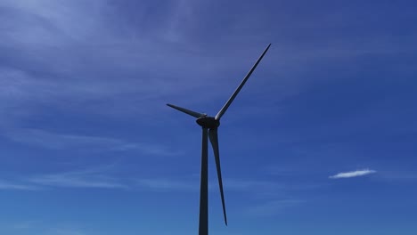 Wind-turbine-spinning-under-a-bright-blue-sky,-shot-from-a-low-angle