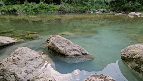 This-serene-stock-footage-captures-a-tranquil-little-river-with-a-slow-water-flow,-surrounded-by-lush-greenery