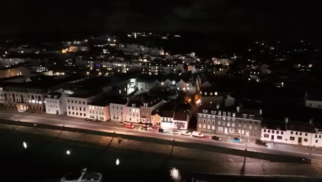 Drone-flight-at-night-along-Glategny-Esplanade-St-Peter-Port-Guernsey-towards-St-Julian’s-Avenue-with-town-in-background-and-illuminated-Elizabeth-College