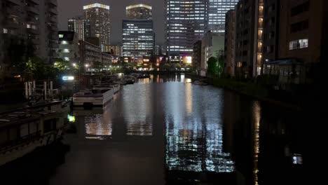 Stadtkanal-Bei-Nacht-Mit-Beleuchteten-Gebäuden-Und-Booten,-Die-Sich-Im-Wasser-Spiegeln