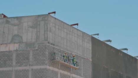 Workers-labouring-on-a-suspended-platform-at-a-construction-site-during-a-hot-summer-day-in-Dubai,-United-Arab-Emirates