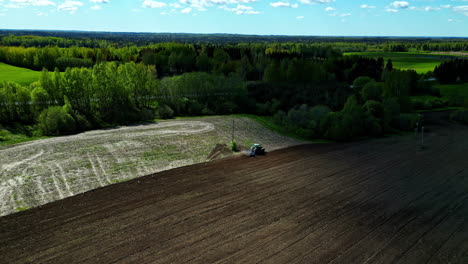 Aerial-rural-landscape-of-a-truck-working-in-agricultural-fields-soil-green-forest-skyline-background