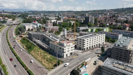 Drone-slowly-flying-away-from-construction-site-with-newly-built-structures-and-revealing-the-skyline-of-a-beautiful-city-in-Switzerland