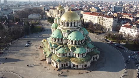 Clip-Aéreo-Orbital-De-Drones-Dando-Vueltas-Alrededor-De-La-Catedral-De-Alexander-Nevsky-En-El-Sentido-Contrario-A-Las-Agujas-Del-Reloj-Bajo-El-Sol-De-Invierno-Con-La-Ciudad-De-Sofía,-Bulgaria-Al-Fondo