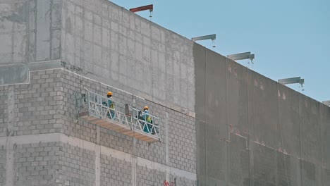 Workers-labouring-on-a-suspended-platform-at-a-construction-site-during-a-hot-summer-day-in-Dubai,-United-Arab-Emirates