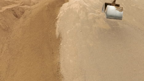An-aerial-view-of-an-excavator-scoop-digging-into-a-sand-pile,-capturing-the-texture-of-the-sand
