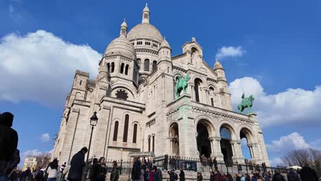 Crowd-of-people-at-Sacre-Coeur-with-clouds-moving-in-blue-sky,-Montmartre-in-Paris,-France