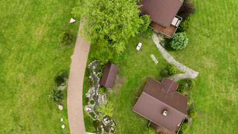 A-top-down-aerial-view-of-a-property-with-a-house,-pathways,-and-a-small-garden-area,-surrounded-by-green-lawns