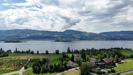 Vista-Panorámica-De-Feldbach-Y-Las-Islas-En-El-Lago-De-Zurich-Con-Exuberantes-Colinas-Verdes-Y-Cielo-Nublado