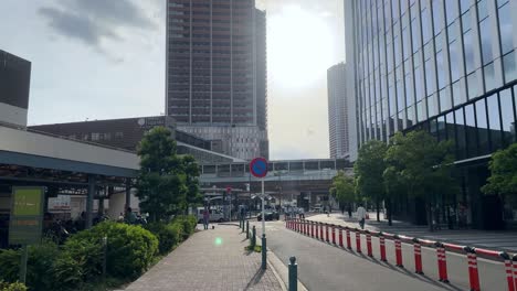 Sunny-city-street-with-tall-buildings,-trees,-and-people-walking-on-a-clear-day