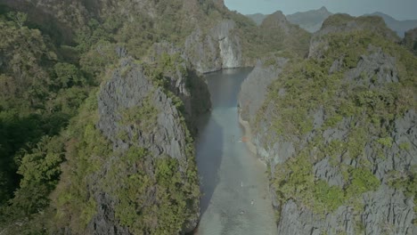 Tourists-in-kayaks-in-calm-water-by-cliffs-in-Philippines,-aerial-push-in