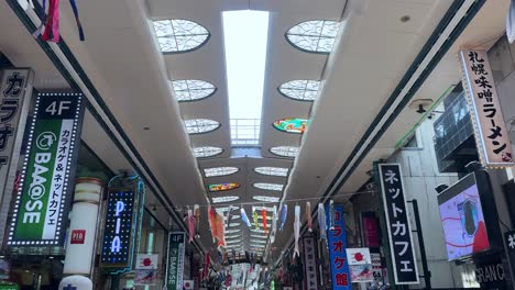 Cometas-De-Peces-De-Colores-Colgando-En-Una-Vibrante-Galería-Comercial-Con-Carteles-Luminosos-Y-Claraboyas