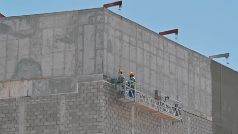 Labourers-are-working-on-a-suspended-platform-at-a-construction-site-in-Dubai,-United-Arab-Emirates