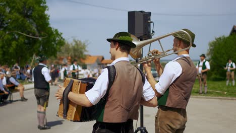 Jährliche-Traditionelle-Bayerische-Maifestfeier-Mit-Musikern,-Menschen,-Maibaum,-Peitschen,-Lederhosen