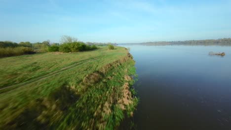 FPV-Ansicht-Von-Einer-Schnell-Fliegenden-Drohne-über-Dem-Flussufer-An-Einem-Sonnigen-Tag